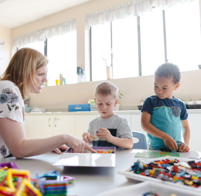 An early childhood educator works with two young boys at a table