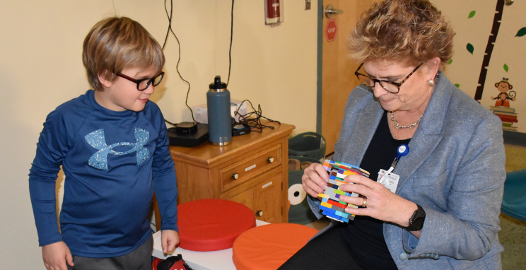 A child watches as an adult wearing a professional blazer and hospital identification badge plays with a colorful toy.